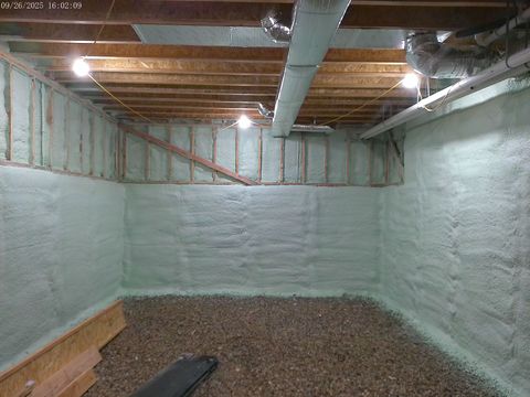 Basement walls and ceiling insulated with light green foam, a gravel floor, and exposed wooden beams.