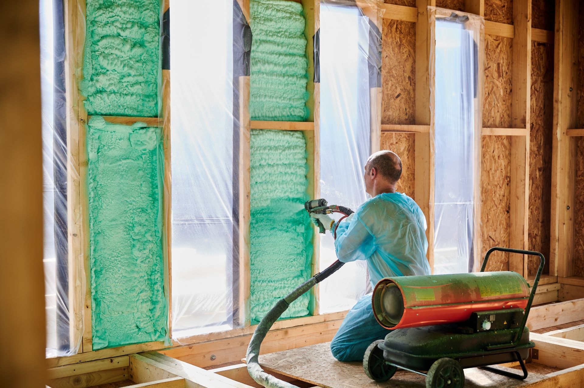 Man sprays green insulation into a wall frame in a construction setting.