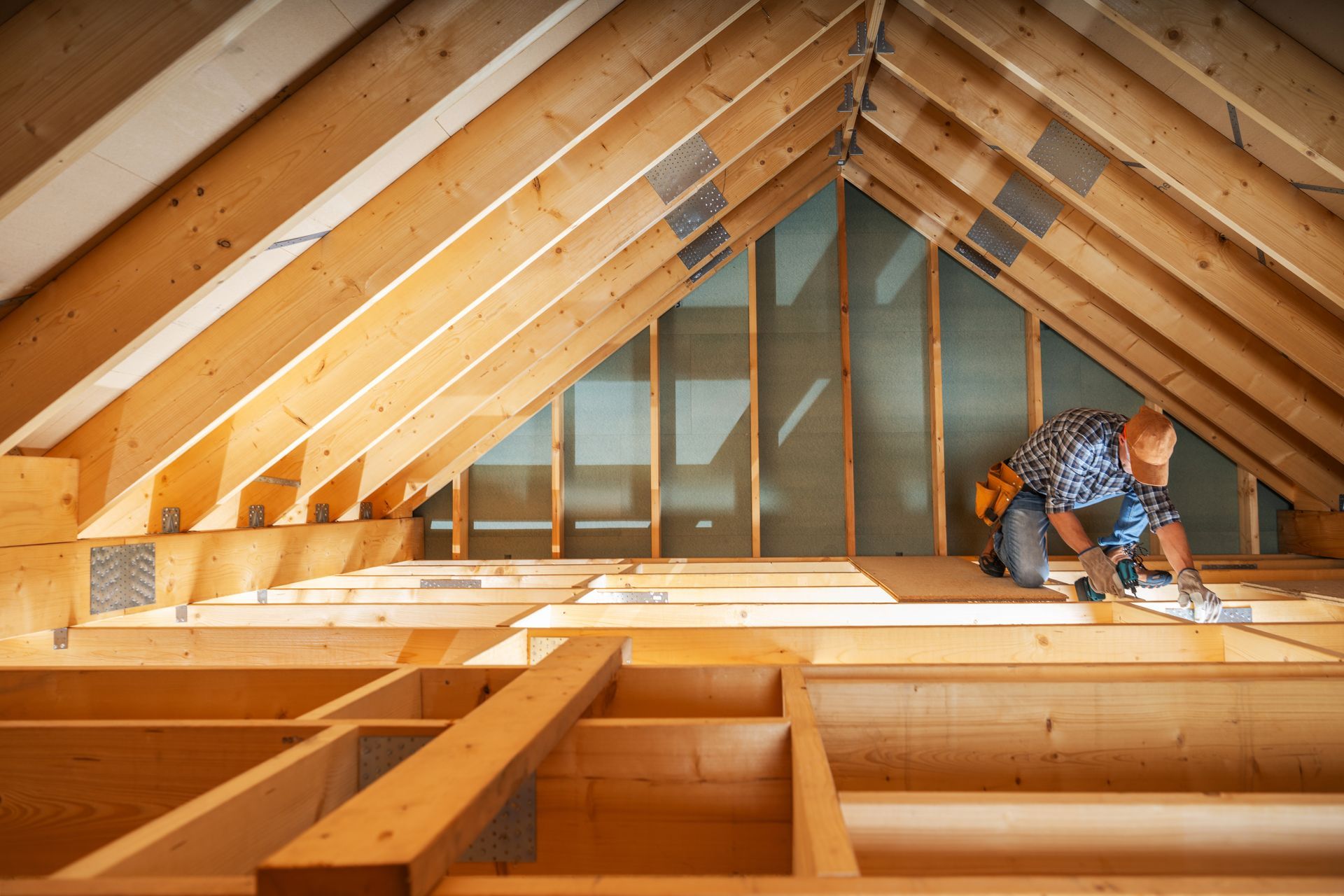 A person working on a wooden attic floor, surrounded by exposed rafters and beams.