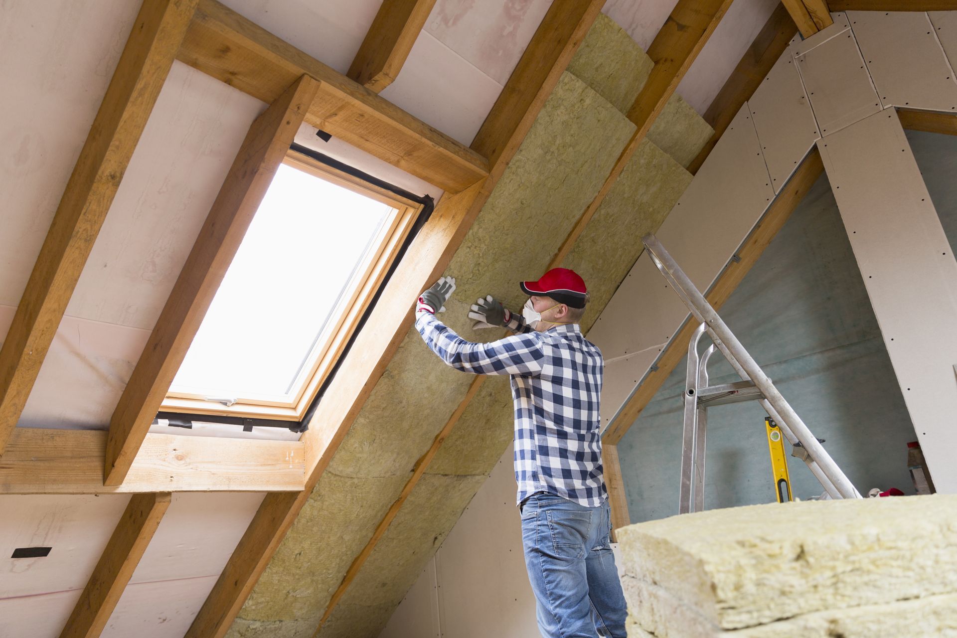 Worker installing insulation in an attic with a skylight.