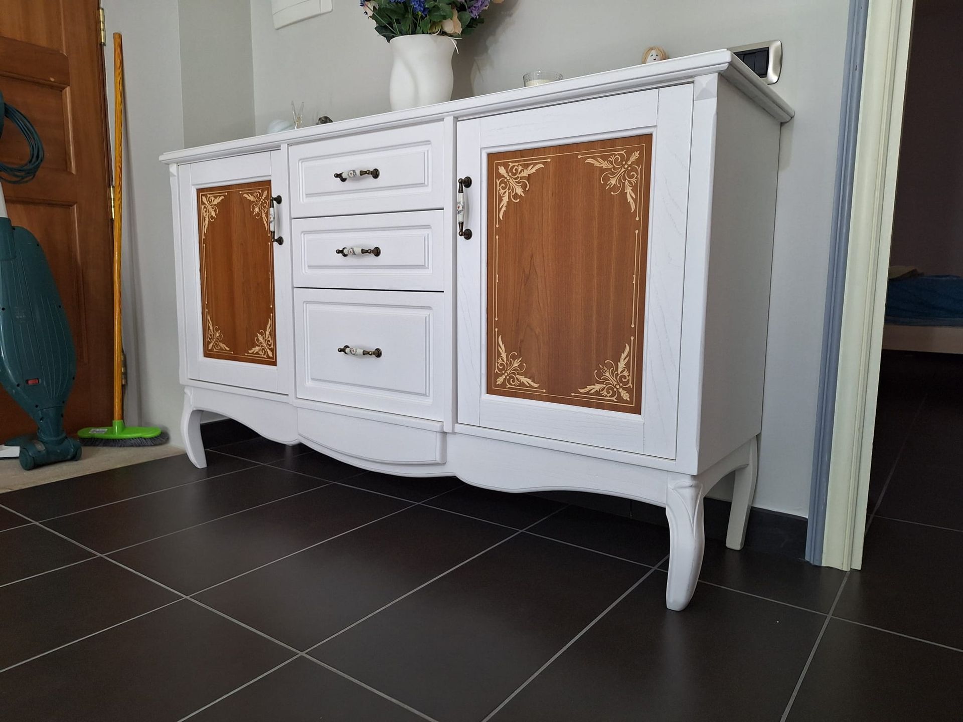 Una cassettiera bianca e marrone è appoggiata sul pavimento piastrellato di una stanza.