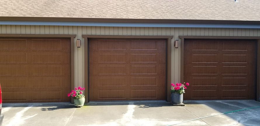 A brick garage with a brown garage door is next to a house.