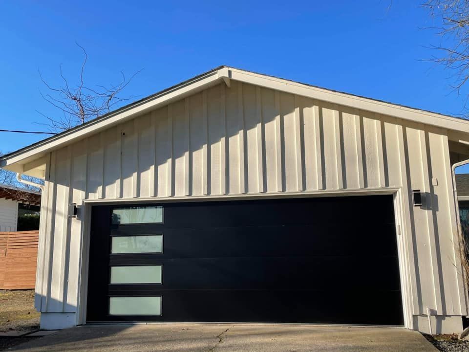 A white garage with a black garage door and a blue sky in the background.