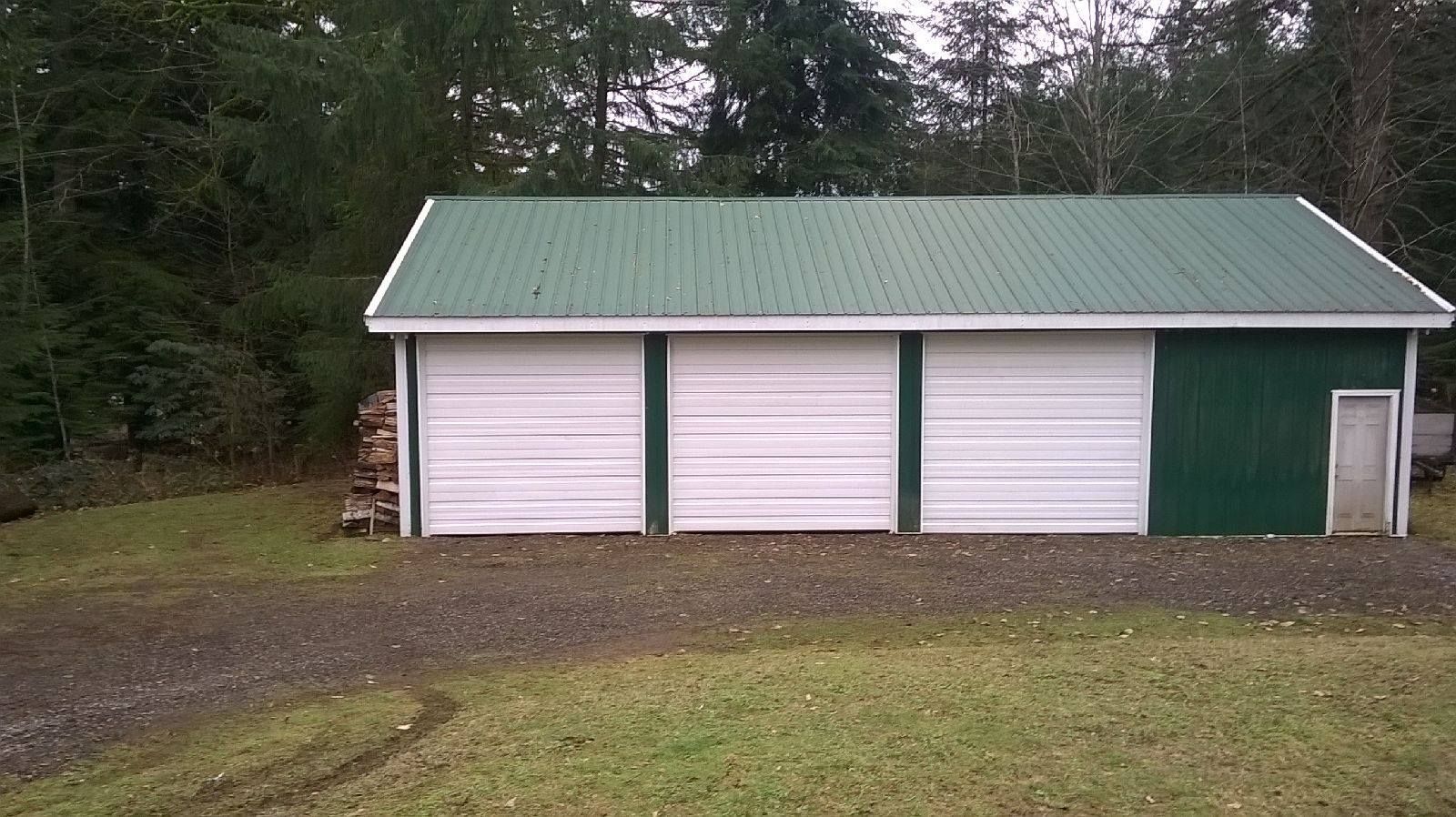 A garage with a green roof and white doors is sitting in the middle of a grassy field.