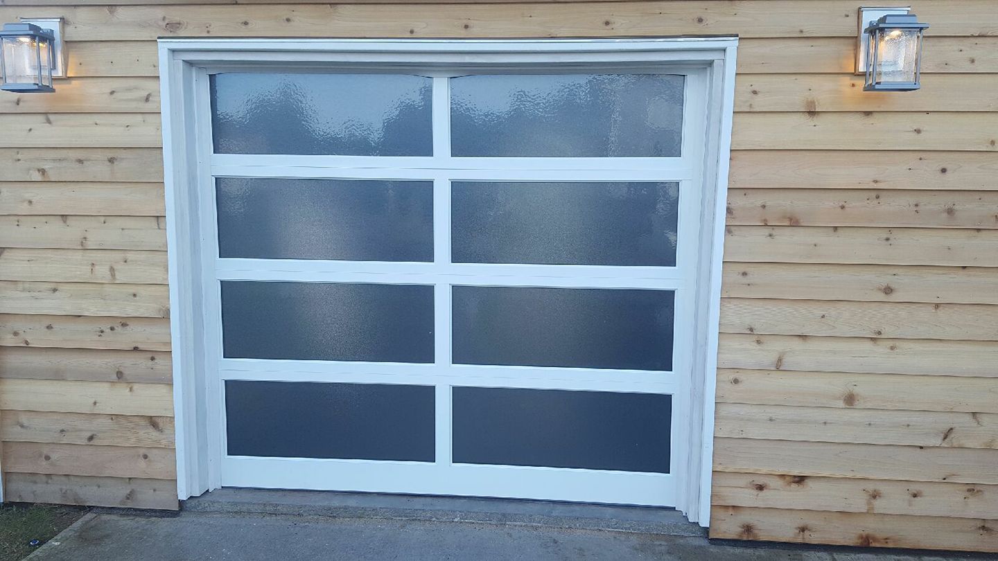 A white garage door is sitting on the side of a wooden house.