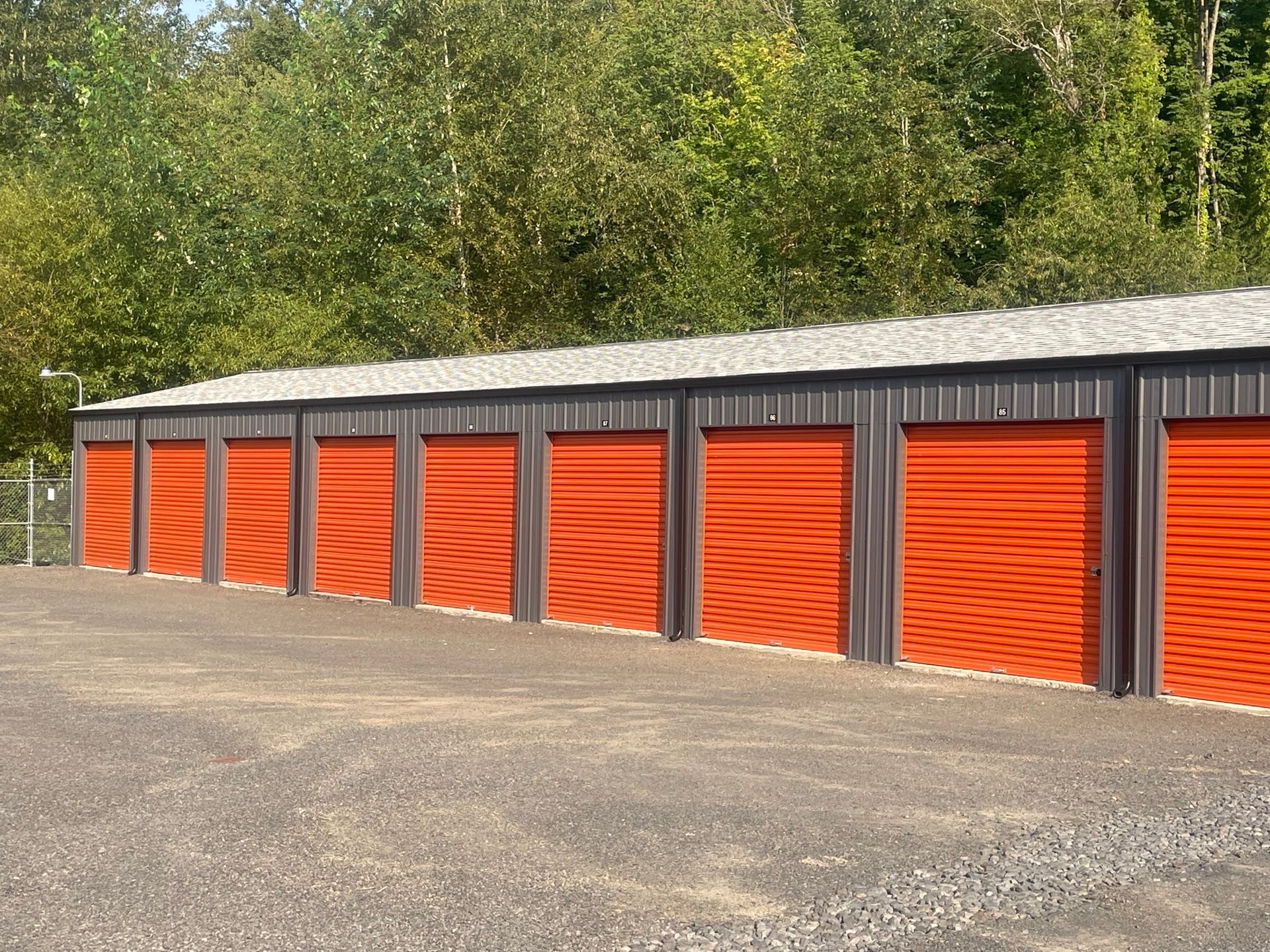 A row of storage units with orange doors are lined up in a parking lot.