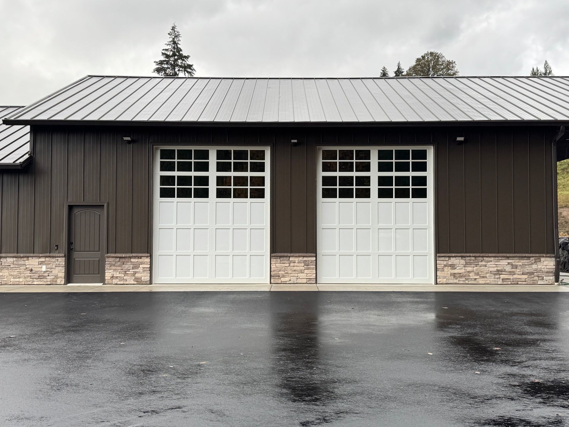 A large garage with two white garage doors and a black roof.