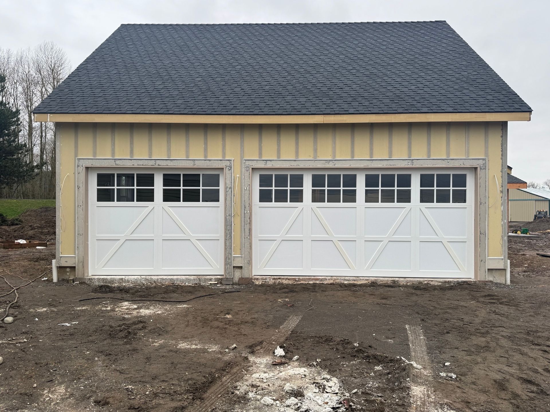 A garage with two white garage doors and a black roof is sitting in the middle of a dirt field.