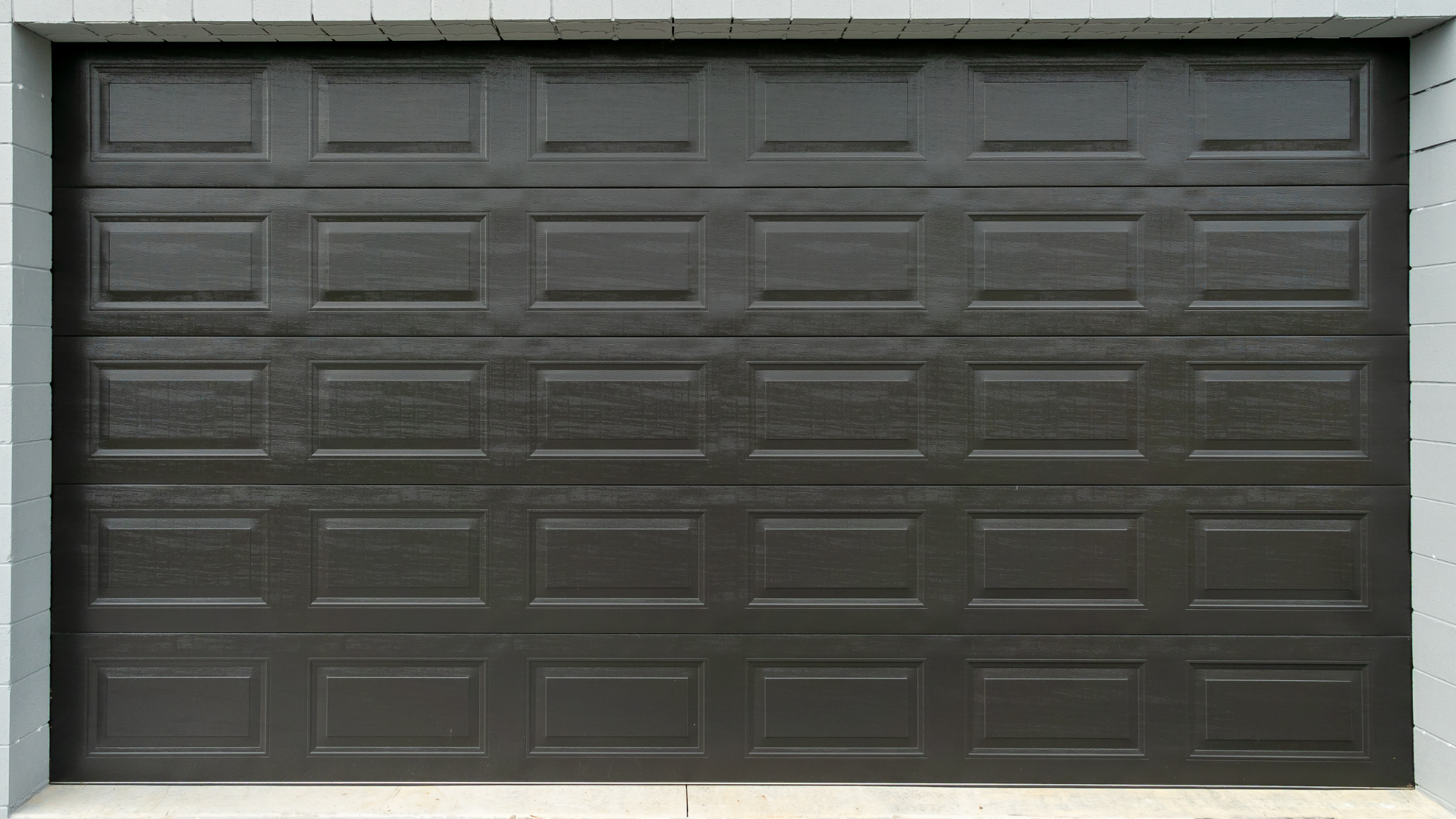A close up of a black garage door on a brick wall.