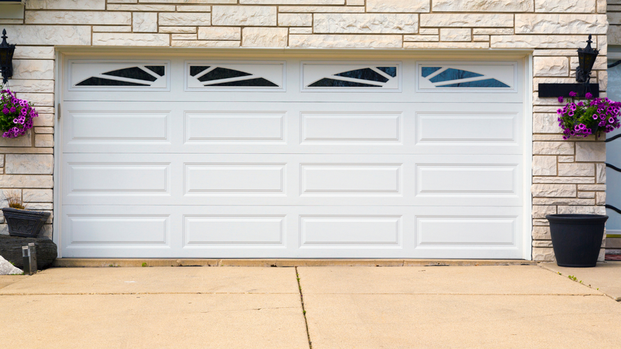 A house with two wooden garage doors and a gravel driveway