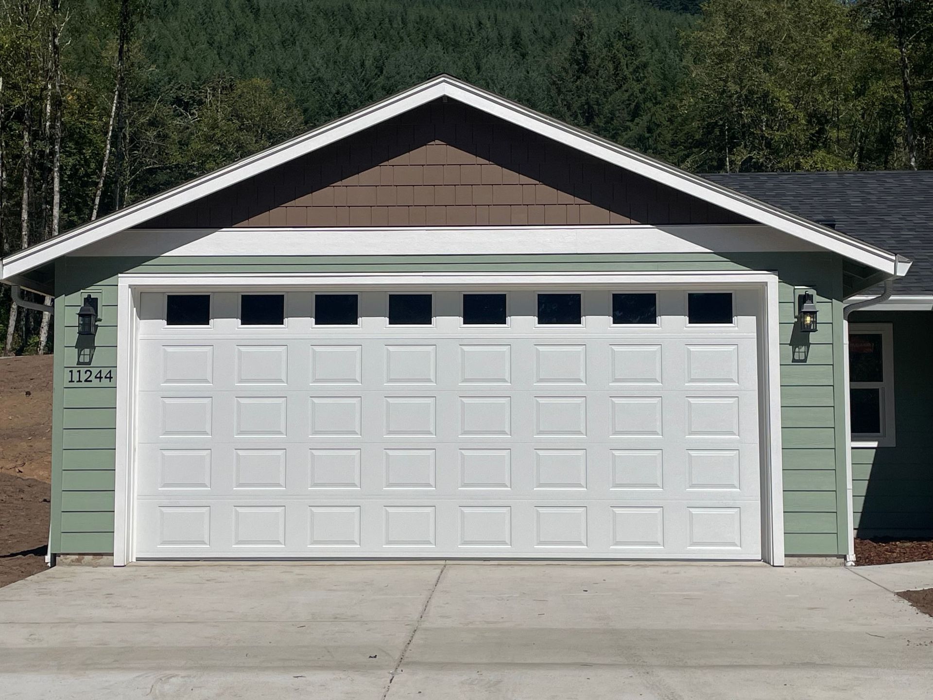 White garage door with windows, green house exterior, set against a wooded background.