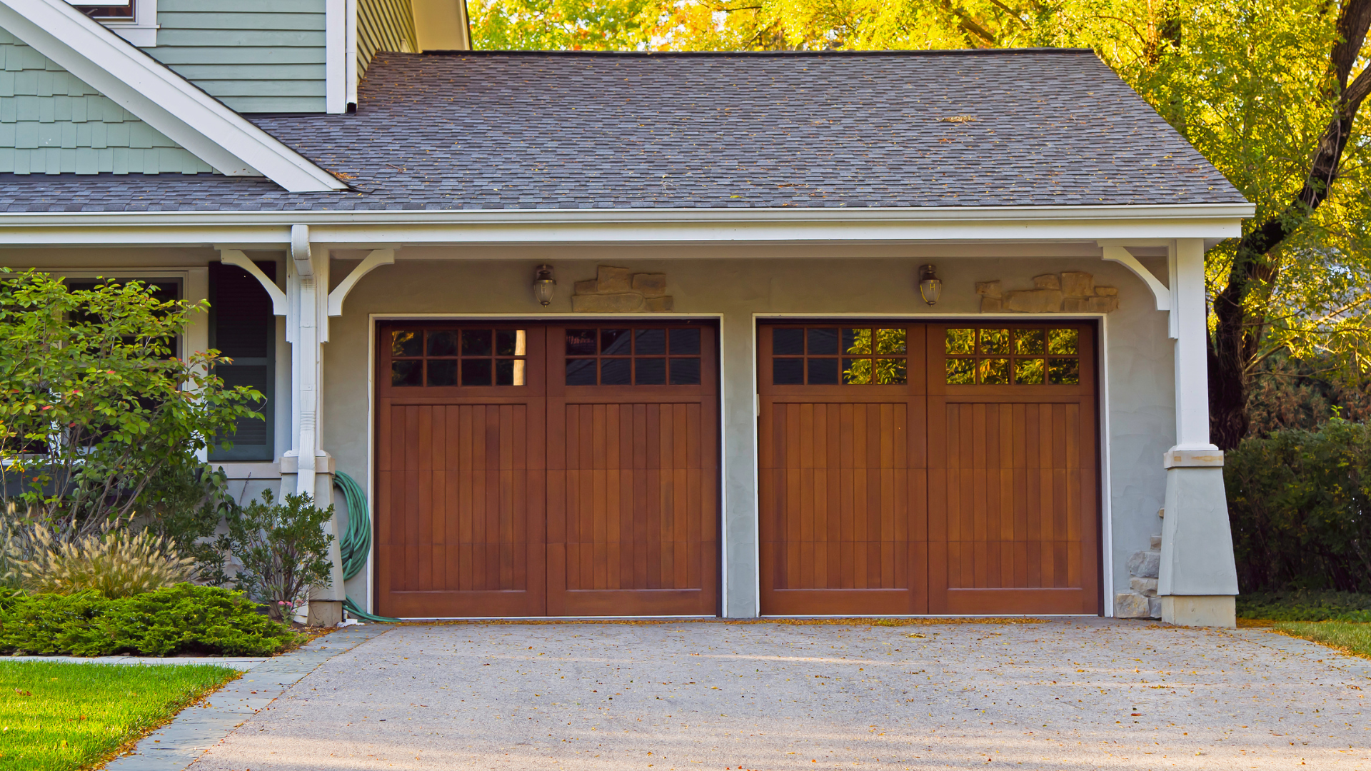 A house with two wooden garage doors and a gravel driveway