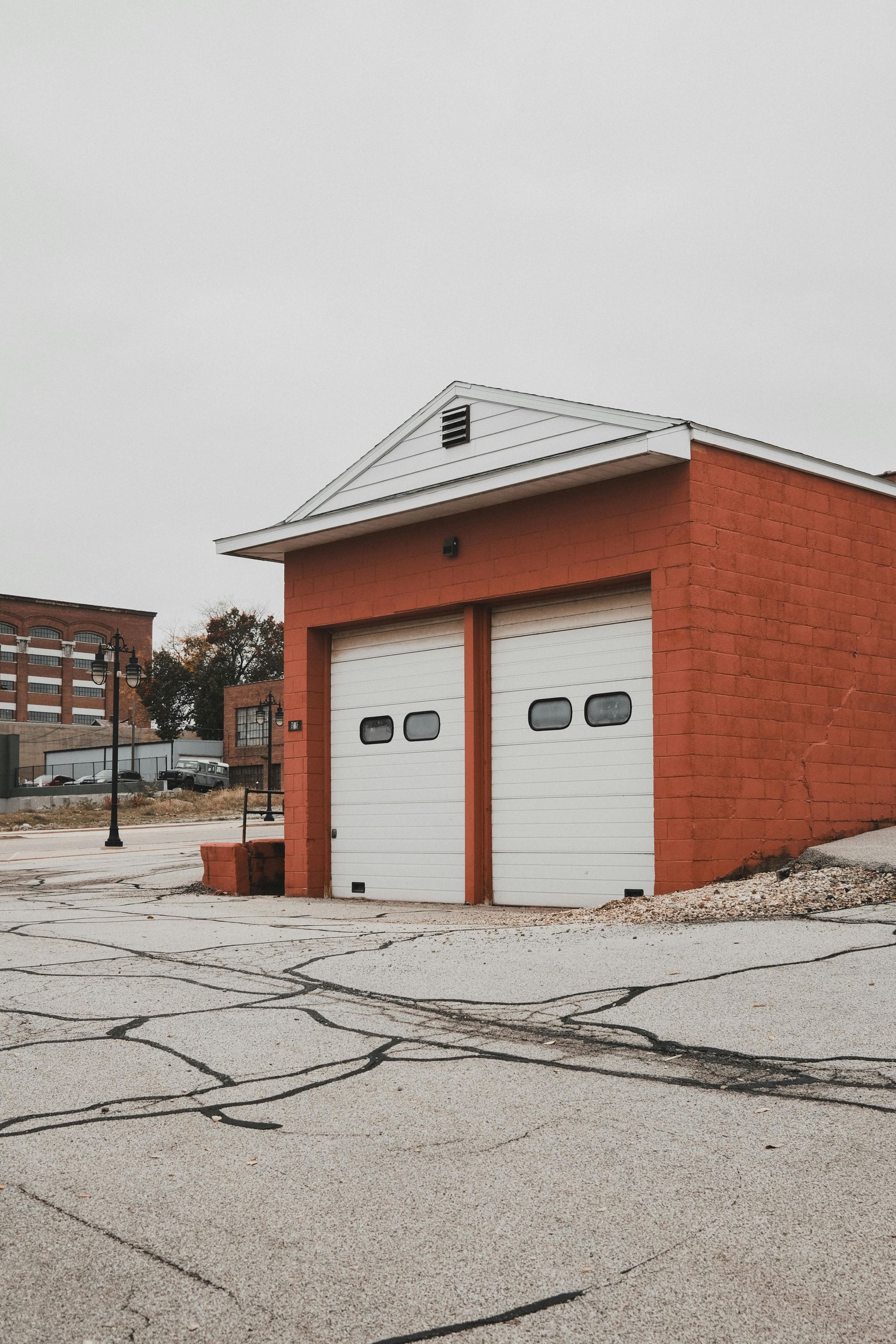 Red brick building with two white garage doors, gray sky.