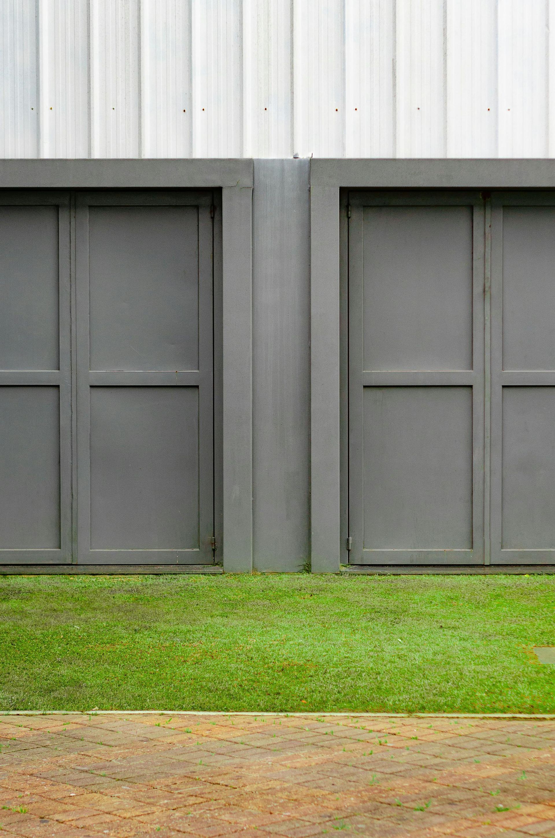 Two gray garage doors are sitting next to each other on a lush green lawn.