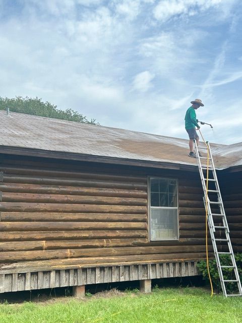 Person pressure washing a log cabin roof from a ladder.
