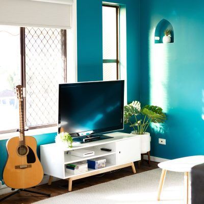 A living room with teal walls, a white TV stand, and an acoustic guitar. A TV sits above the stand.