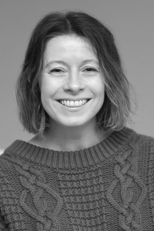 Woman with short hair smiles broadly, wearing a cable-knit sweater.