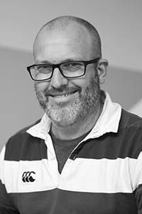 A man with a beard and glasses wearing a striped rugby shirt smiles at the camera.
