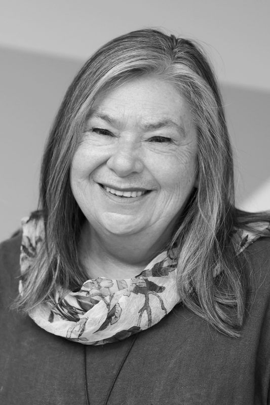 Smiling woman with graying hair and a floral scarf, posing indoors in a studio setting.