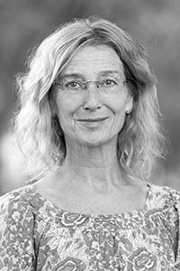 Woman with glasses, wearing a patterned shirt, smiling at the camera.