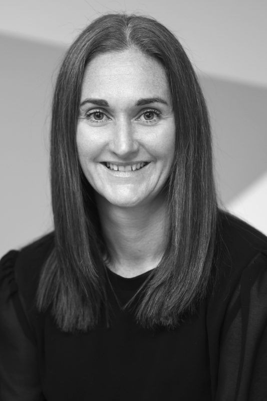 Woman with shoulder-length dark hair smiles at the camera; she wears a black top and is in a well-lit, neutral setting.