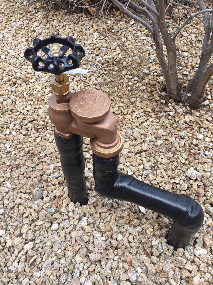 A faucet with a black handle is sitting on top of a pile of gravel.