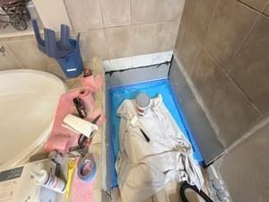 Bathroom floor covered with blue tarp, a white cloth, and tools beside a sink and tiled shower area