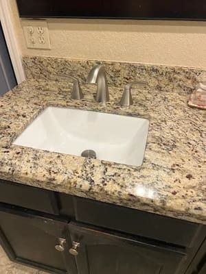 Bathroom vanity with white sink, brushed nickel faucet, and speckled granite countertop.