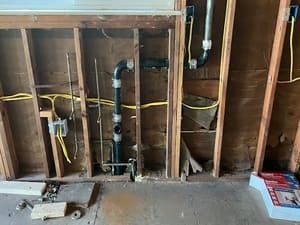 Exposed bathroom wall with plumbing pipes and open studs during renovation