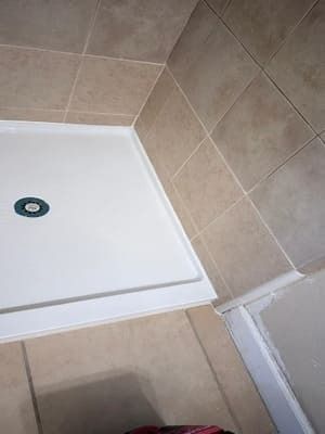 White shower tray with beige tile walls and a visible drain in the corner.