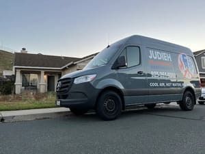 Gray service van parked on a residential street in front of a house at dusk