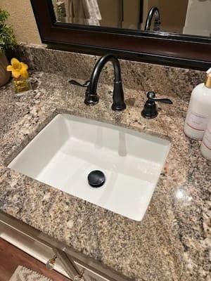 Granite bathroom vanity with white sink, black faucet, and mirror above.