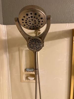 Handheld showerhead mounted on a beige bathroom wall with a hose and holder