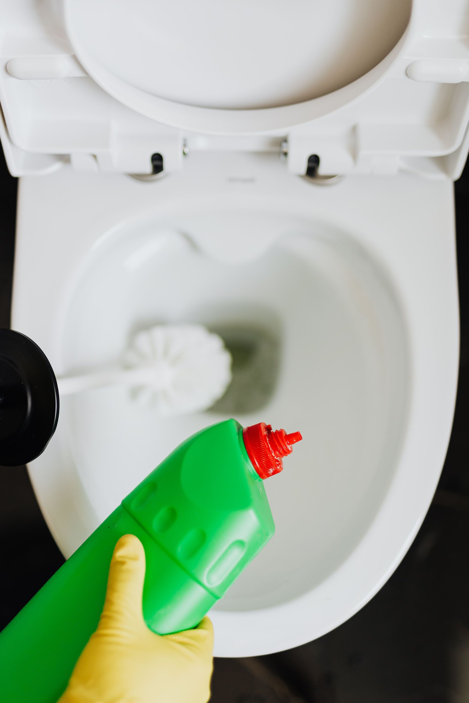 Gloved hand pours red toilet cleaner into a white toilet bowl