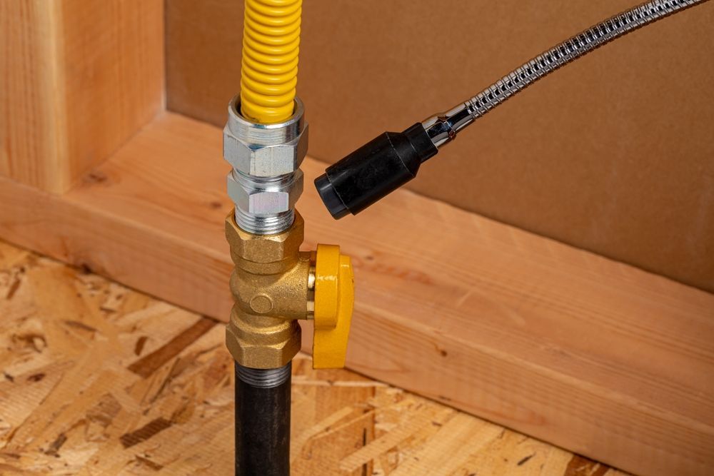Close-up of a yellow gas shutoff valve and pipe connection near a wooden wall and subfloor.