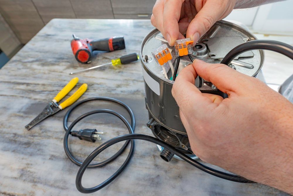 Hands repairing black wiring inside a device on a workbench with tools nearby