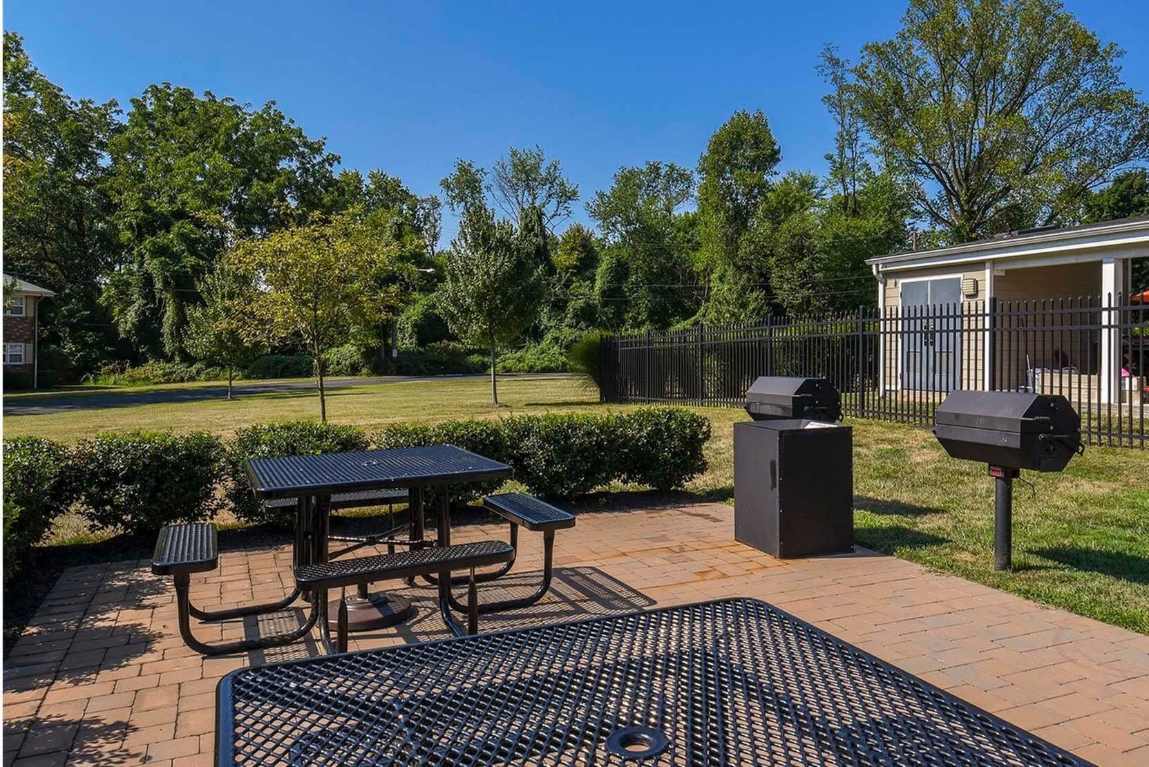 Outdoor community grilling area with a metal picnic table, benches, and two charcoal grills.