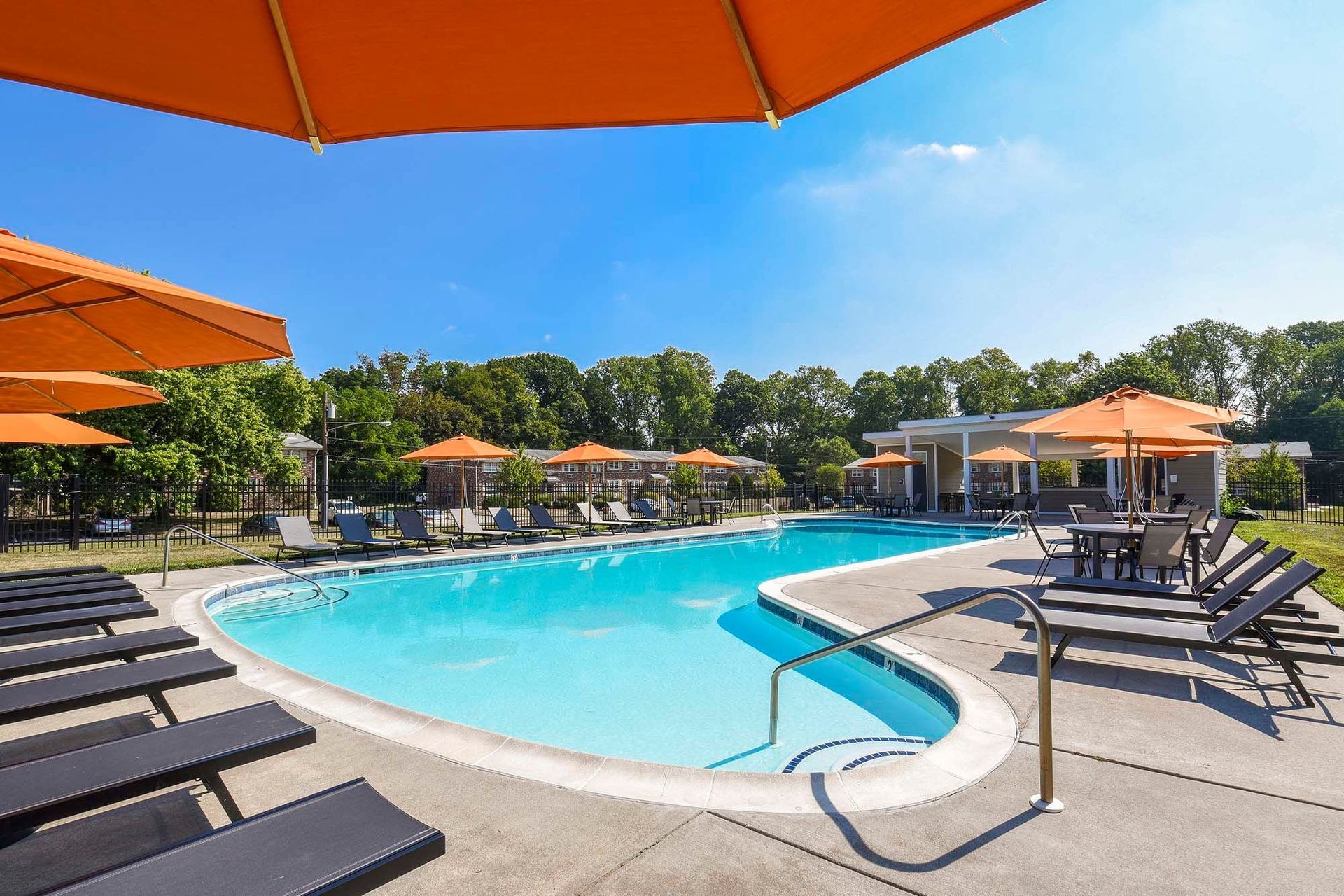 Outdoor apartment community pool with blue water, orange umbrellas, and lounge chairs along the deck.