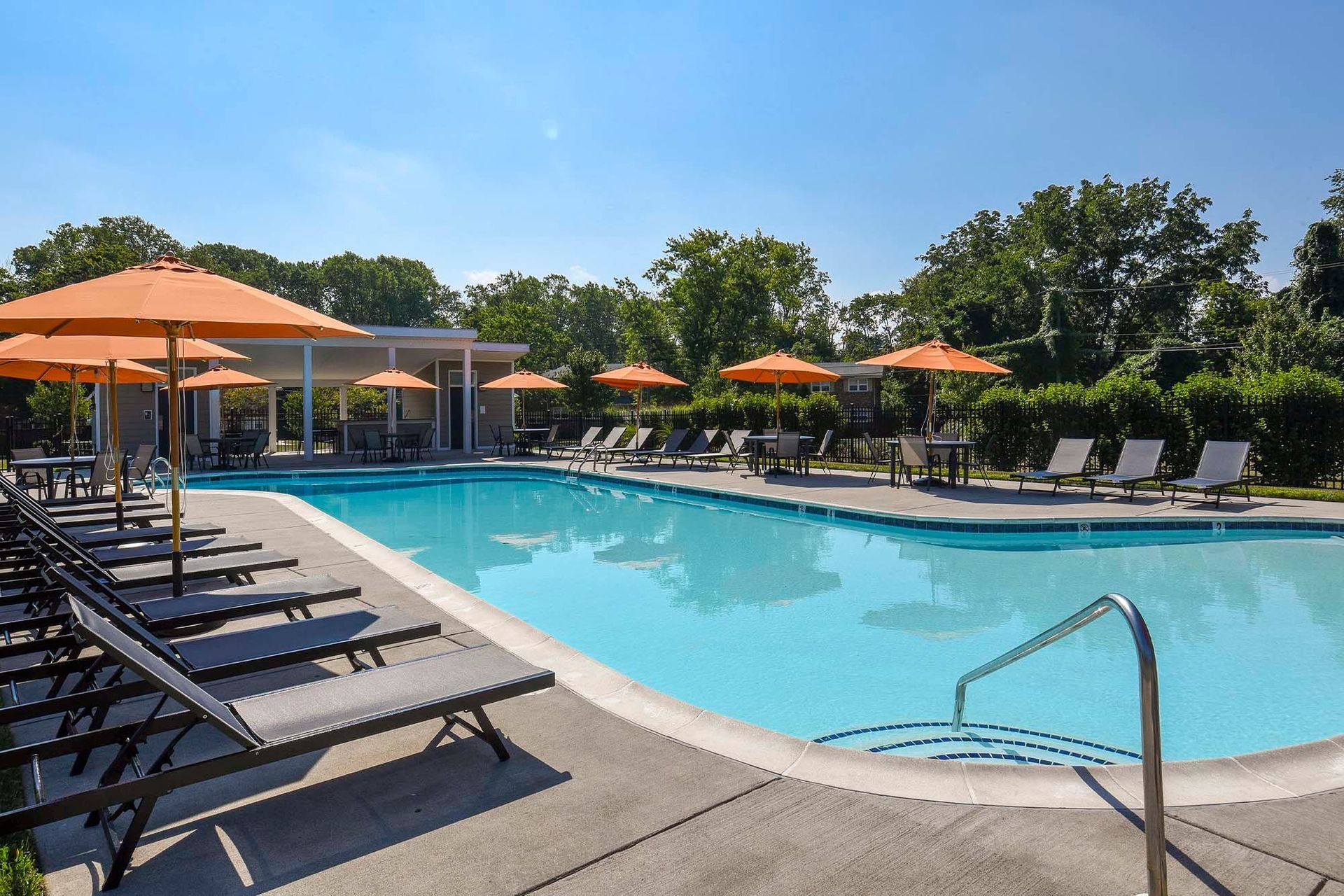 Outdoor apartment pool with lounge chairs and orange umbrellas.