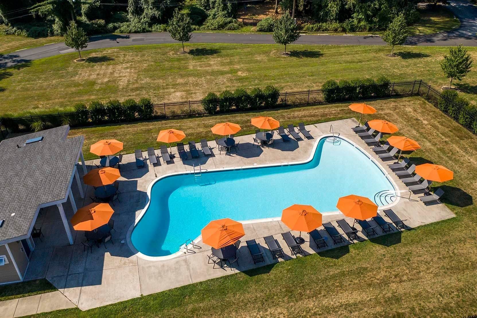 Aerial view of a curvy outdoor pool surrounded by orange umbrellas and lounge chairs at a residential community.