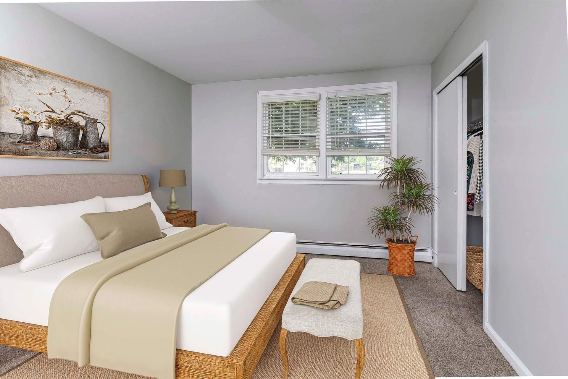 Bedroom in an apartment with a platform bed, neutral bedding, window, bench, and closet.