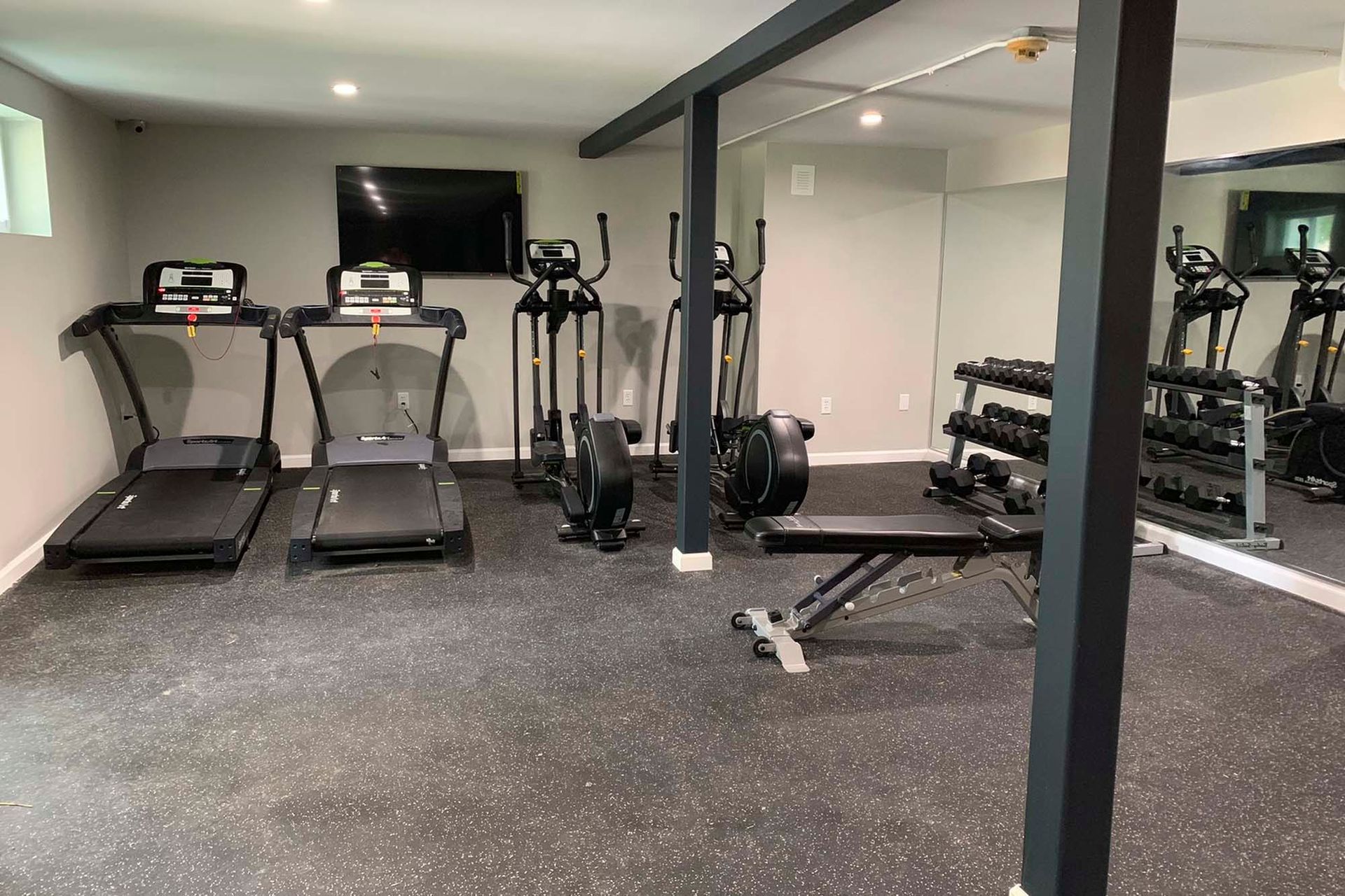 Indoor fitness center with treadmills, elliptical machines, weights, and a bench