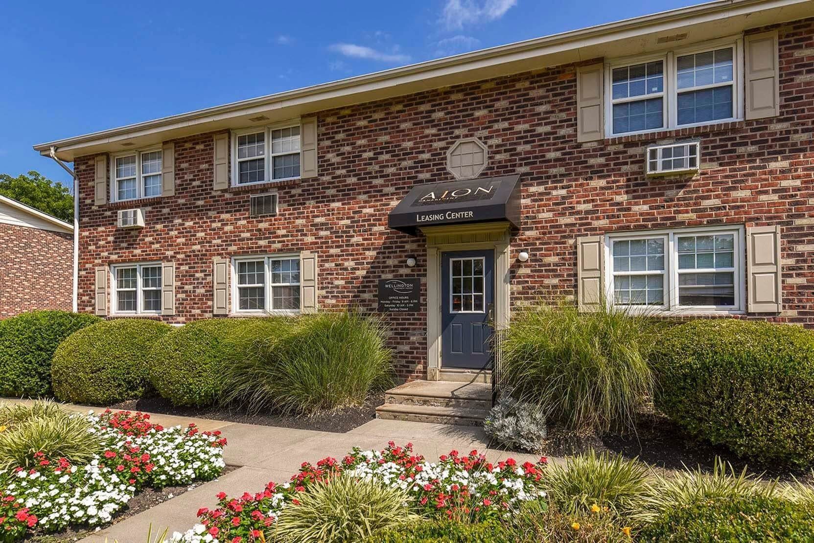 Exterior brick apartment building with leasing center sign and landscaped entrance.