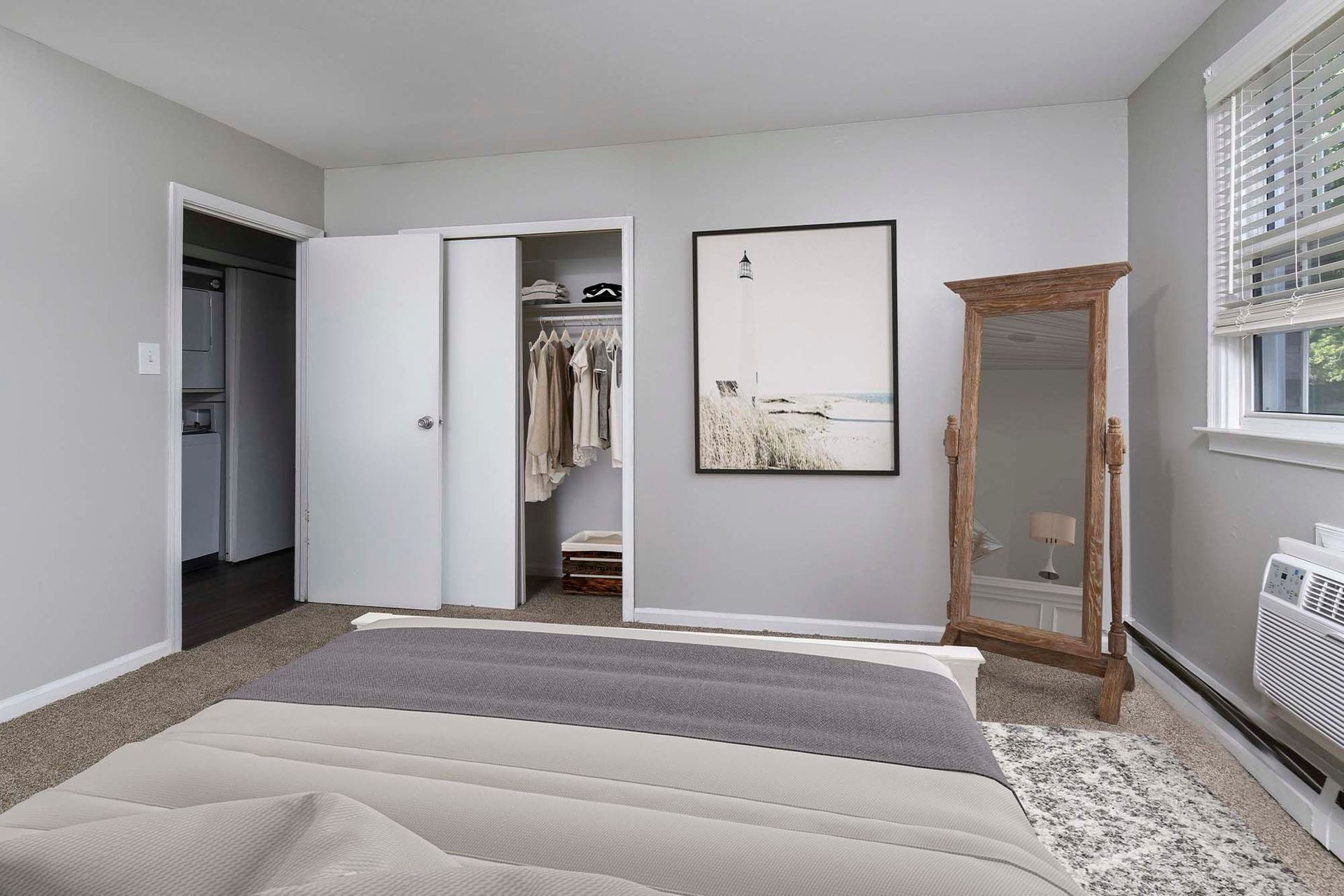 Bedroom with open closet, framed wall art, a tall wooden full-length mirror, and a window AC.