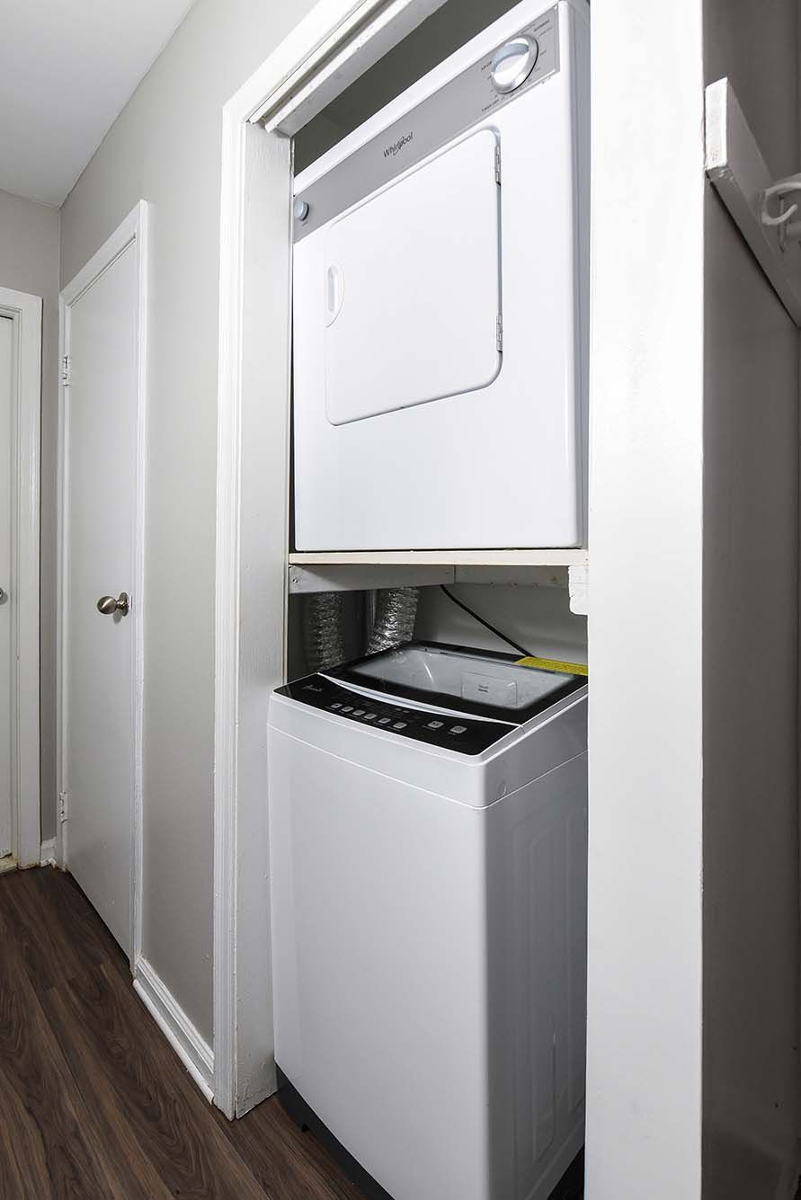 White stacked washer and dryer in a narrow laundry alcove beside a hallway.