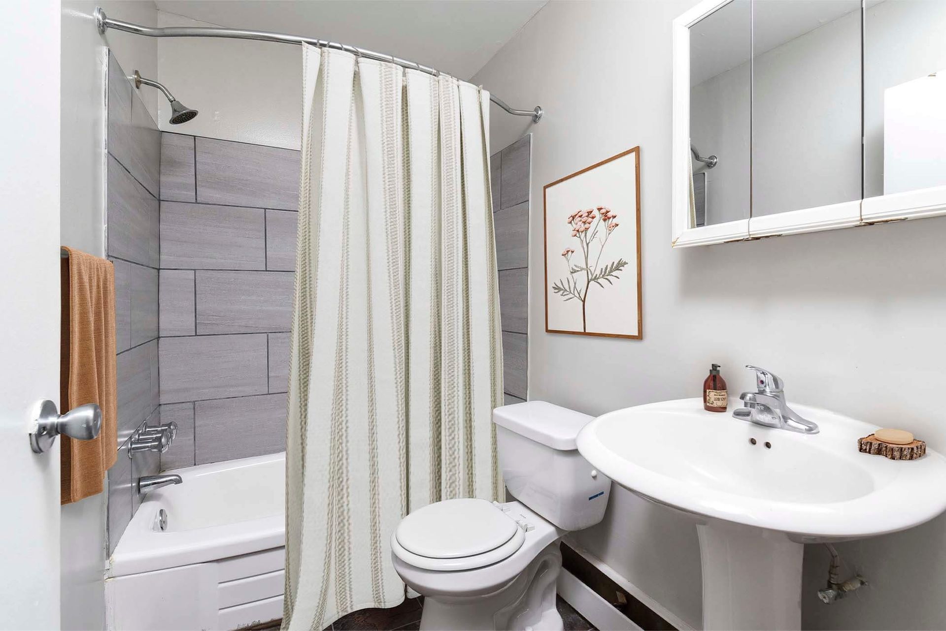Bathroom with a shower/tub combo, striped curtain, gray tile surround, toilet and sink.