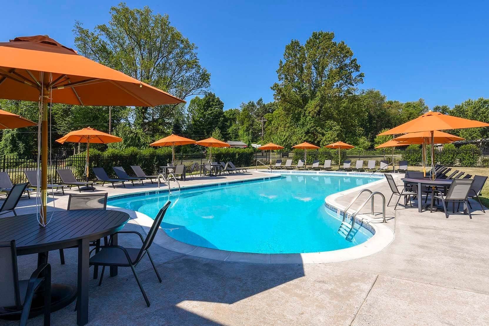 Outdoor community pool with orange umbrellas and lounge chairs.