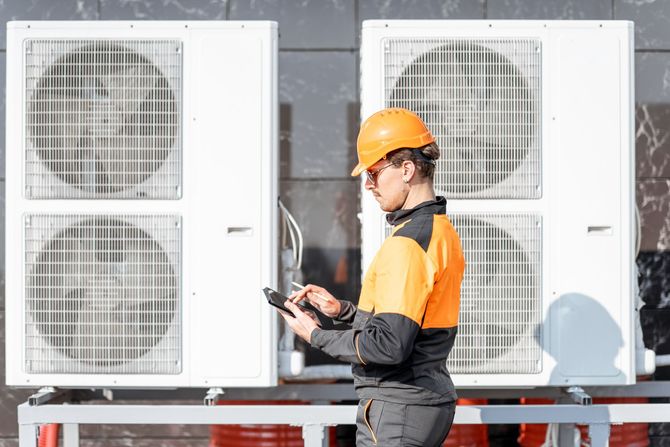 A man is holding a yellow device in front of an air conditioner.