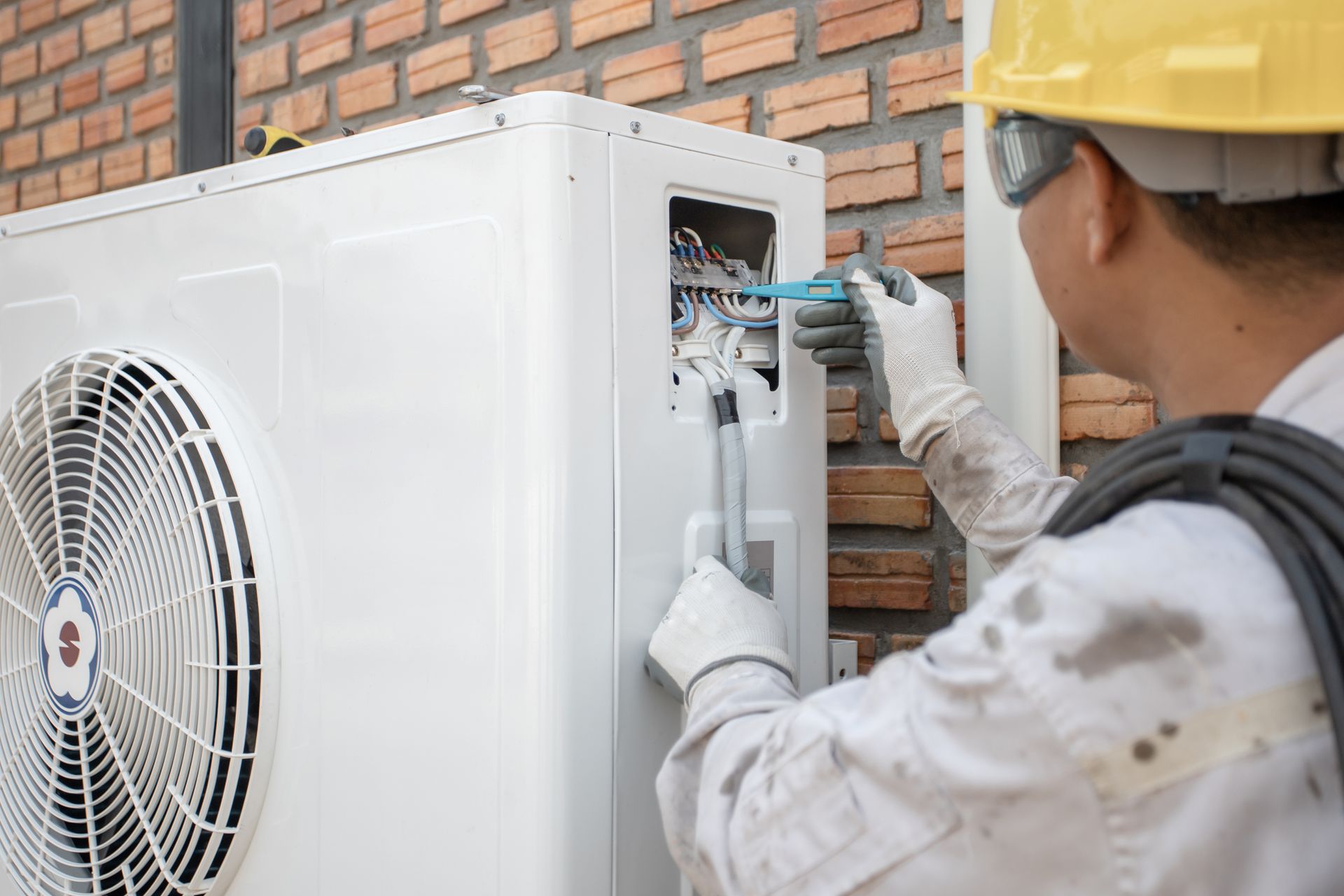 A man is working on an air conditioner outside of a building.