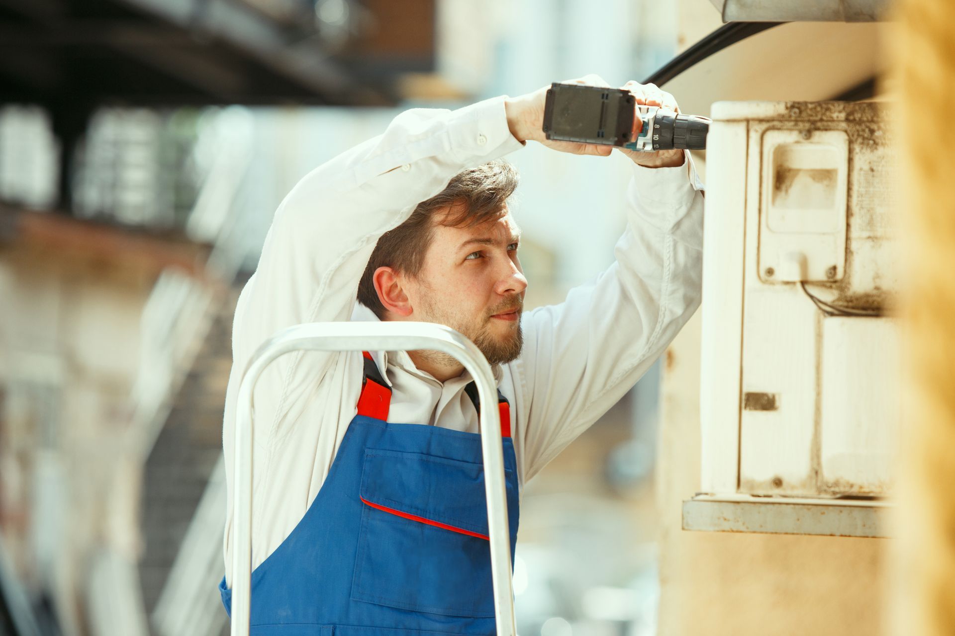 A man is using a drill to fix an air conditioner on the side of a building.